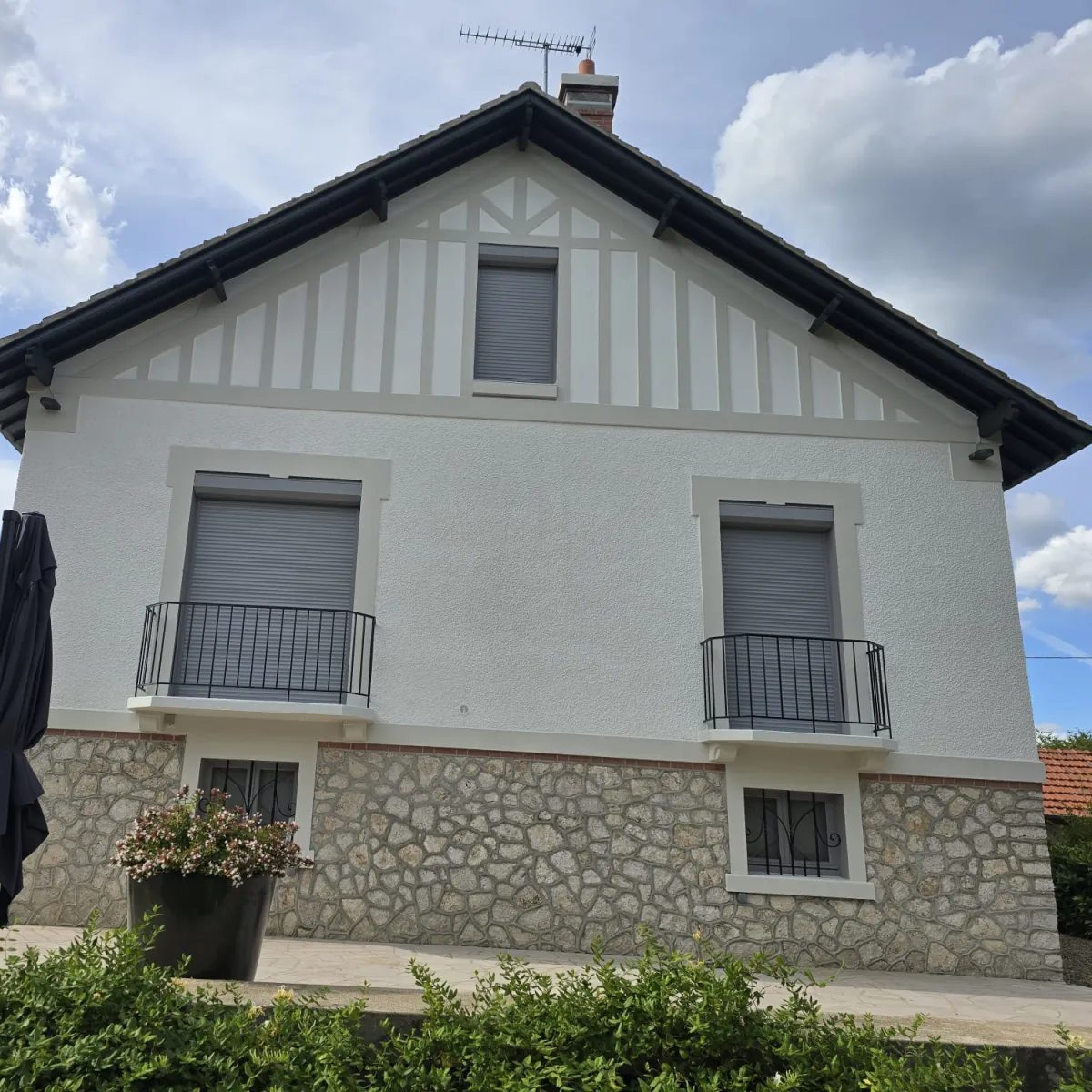 Façade ravalée d'une villa avec pignon à colombages décoratifs et soubassement en pierre